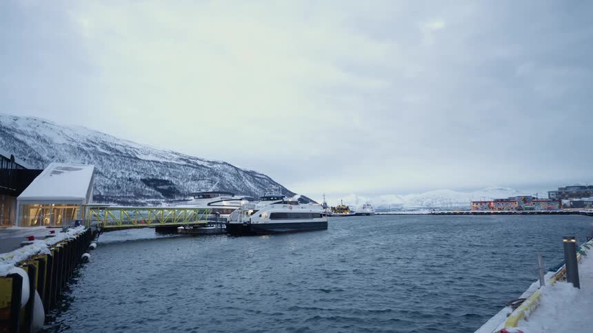 A modern passenger ferry is docked at a snowy pier in a northern harbor on a cold winter day