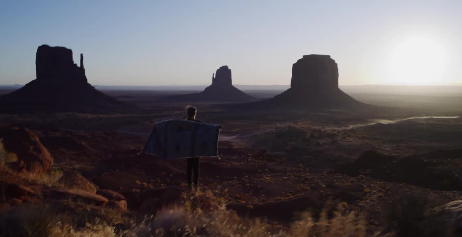 A person unfurls a blanket while watching the sunrise over the majestic landscape of Monument Valley