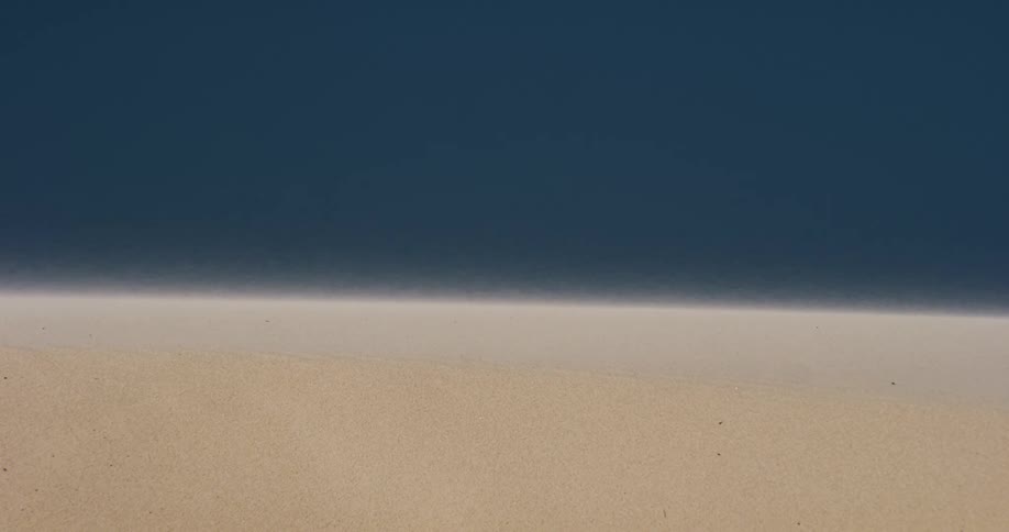 Fine desert sand blows gently across a dune in an abstract, minimalist landscape against a dark blue background