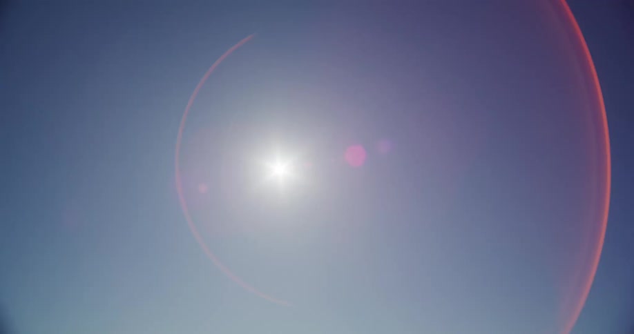 The bright sun casts a beautiful, shifting lens flare across a clear and cloudless blue sky