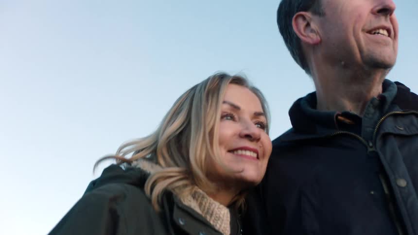 A low-angle close-up of a happy mature couple smiling and cuddling outdoors against a clear sky