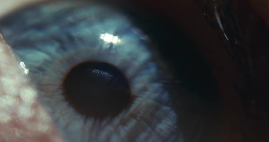 A cinematic macro shot reveals the intricate details of a blue human eye as the eyelid opens