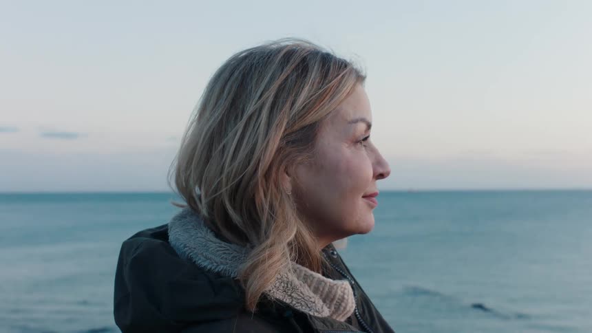 Close up profile of a woman with a serene expression looking out over the calm ocean waters during twilight