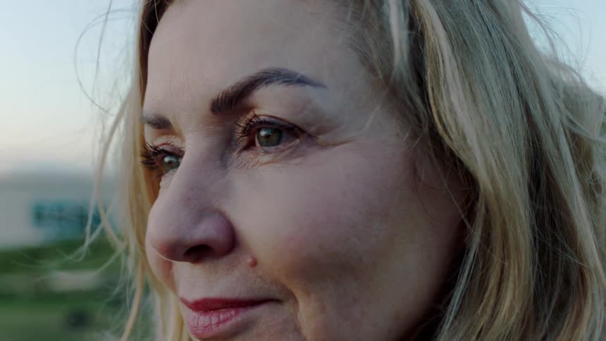 A gentle breeze blows through the hair of a peaceful middle-aged woman as she smiles contentedly in a slow-motion close-up