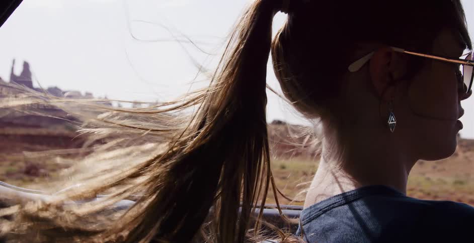 A woman's hair blows in the wind in slow motion as she drives through the desert on a sunny day