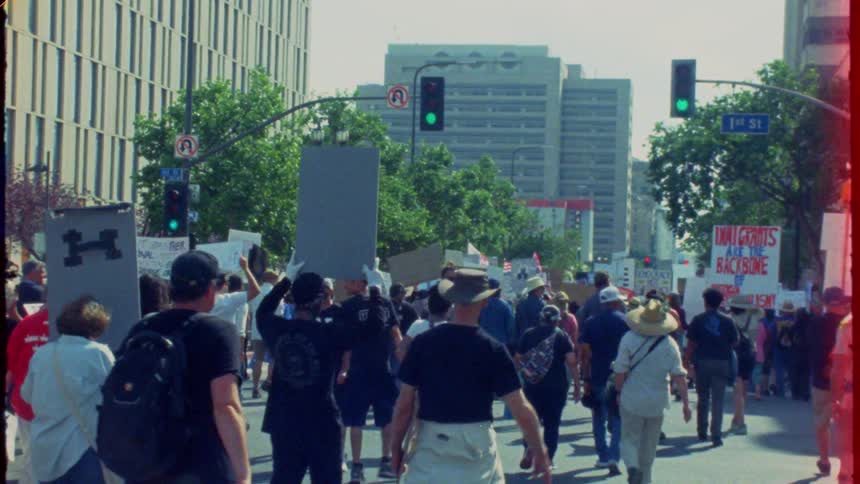 A diverse crowd of activists marches down a city street in a protest for immigrant rights, captured on vintage film