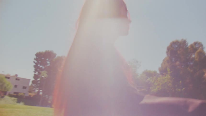 Slow motion shot of a smiling woman with long red hair walking in a sun-drenched park with a strong lens flare