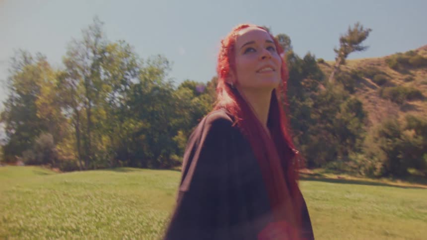 A free-spirited woman with flowing red hair twirls with joy in a sunlit grassy field