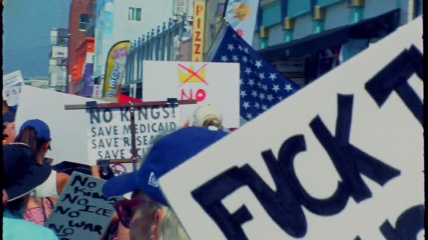 Archival-style footage of an American political protest with anti-establishment signs and a US flag in a crowded street