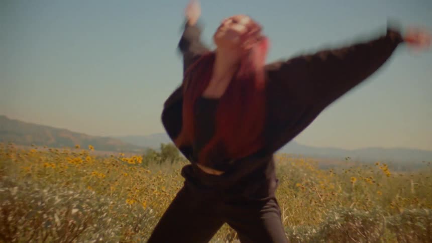 A free-spirited woman with vibrant red hair performs an expressive contemporary dance in a sun-drenched field of yellow wildflowers