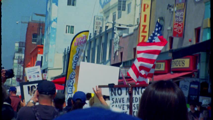 Vintage film footage shows a crowd of protestors marching down a city street waving an American flag and holding signs
