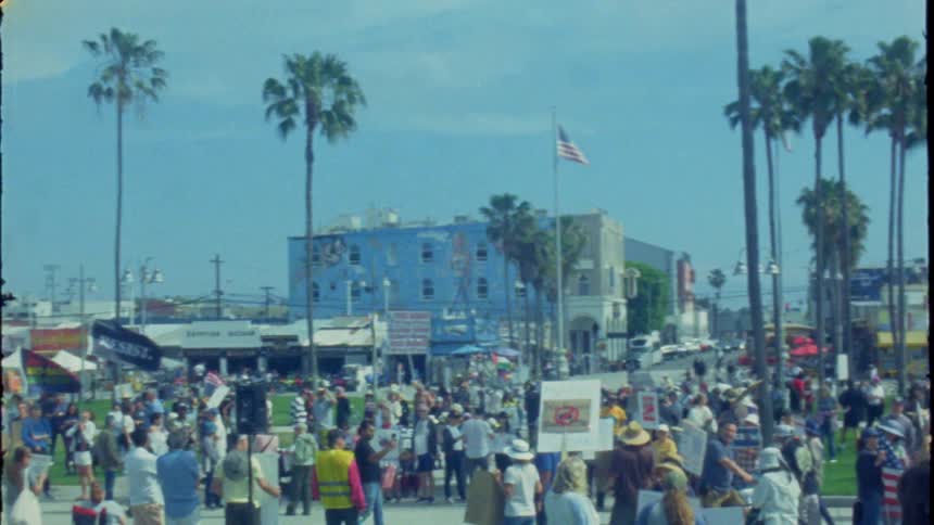 Vintage film footage captures a diverse crowd of activists at a sunny political rally in Venice Beach