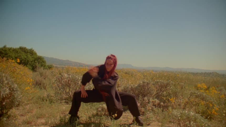 An expressive dancer with vibrant red hair performs a powerful slow-motion dance in a sunny wildflower meadow