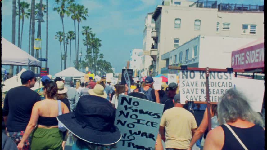 Vintage film captures a political protest march with signs and banners down the sunny Venice Beach boardwalk in California
