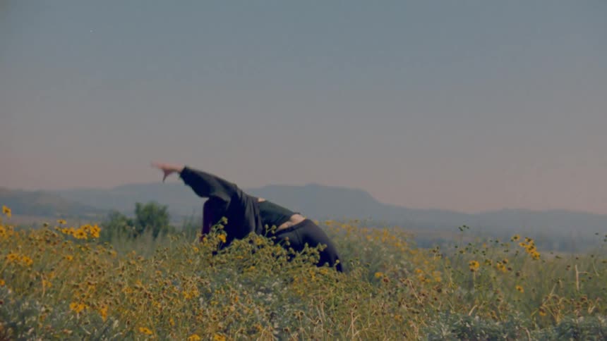 A free-spirited woman with vibrant red hair performs an expressive dance in a sunlit field of yellow wildflowers
