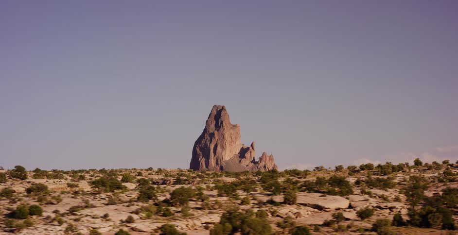A cinematic tracking shot slowly approaches the iconic Agathla Peak rising from the vast, arid desert landscape of Arizona