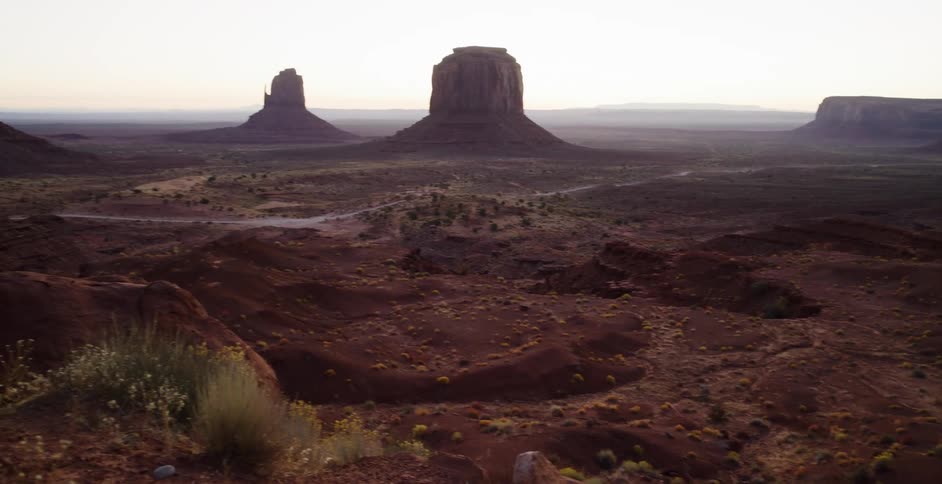 A woman wrapped in a blanket sips a warm beverage on a cliff overlooking the iconic buttes of Monument Valley at sunrise