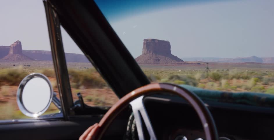 View from the passenger seat of a classic car driving through the iconic Monument Valley desert landscape