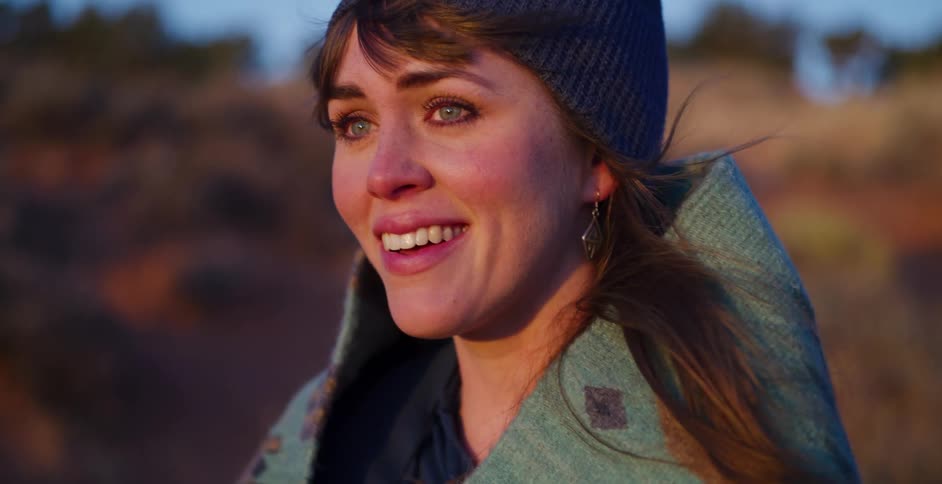 A close-up of an emotional young woman smiling with tears in her eyes as the sunset light warms her face