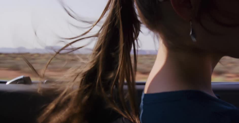 The wind blows through a woman's long ponytail as she enjoys a scenic drive through the desert in slow motion