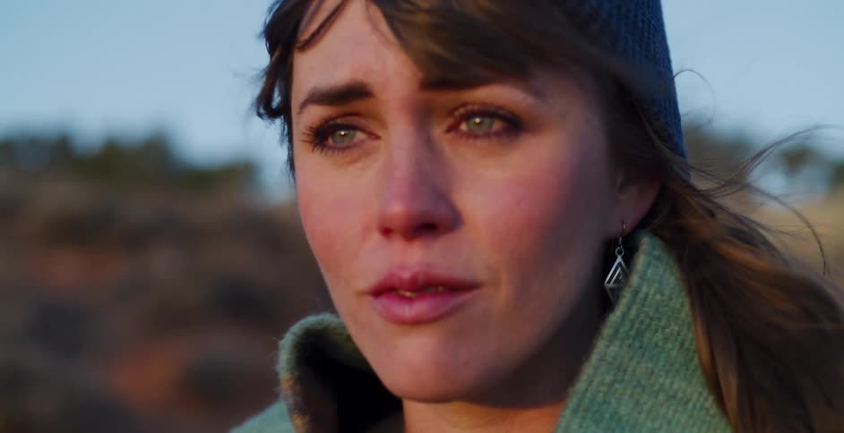 A sorrowful woman wrapped in a blanket looks into the distance with tears in her eyes during a windy sunset