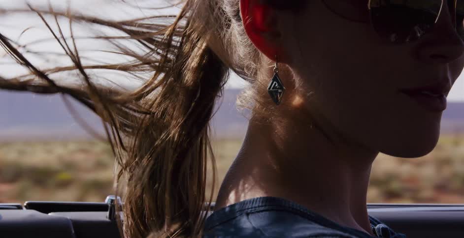 A woman's ponytail whips in the wind in slow motion as she enjoys a sunny drive in a convertible