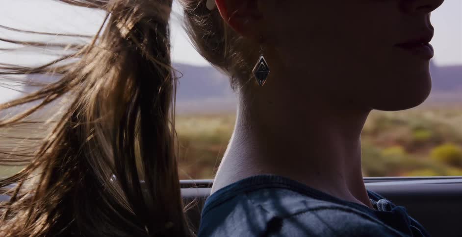 Slow motion close-up of a woman's ponytail blowing in the wind as she looks out of a car window during a scenic drive