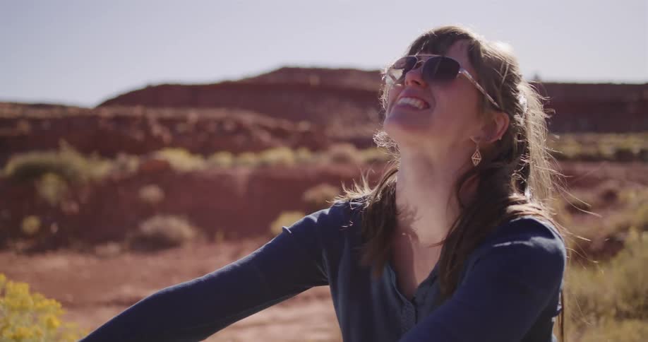 A happy woman in sunglasses flips her hair back in slow motion while enjoying the sunshine in the desert