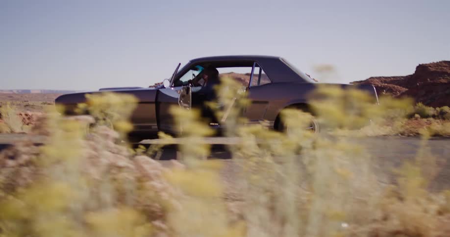 A determined woman push-starts her vintage Ford Mustang on a remote desert highway and jumps in as it rolls