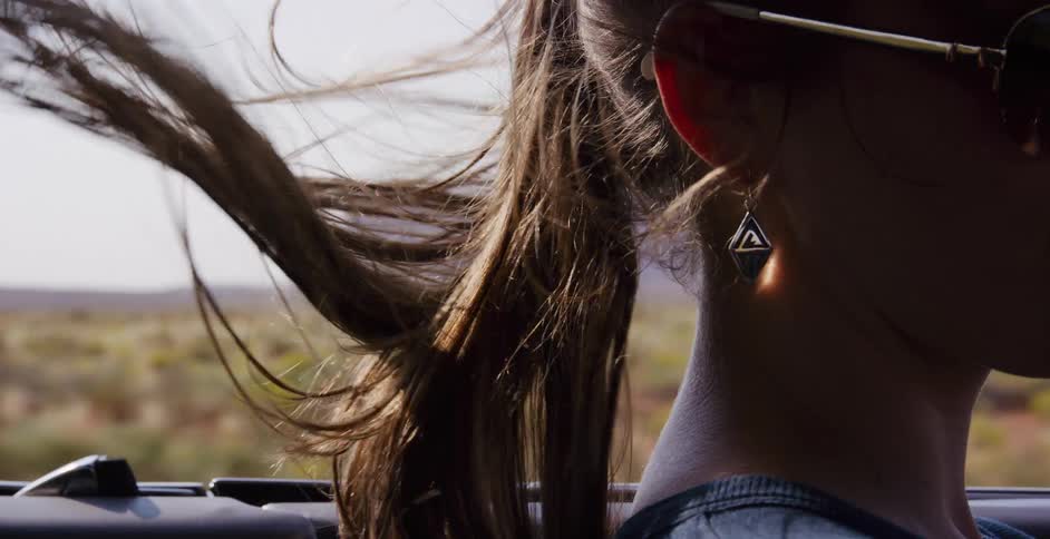 Cinematic slow motion shot of a woman passenger's ponytail blowing in the wind during a road trip through a sunny desert