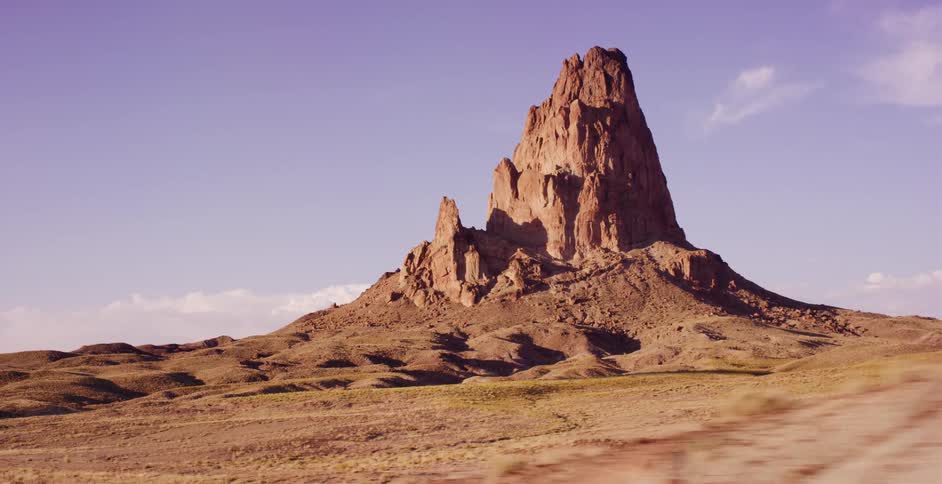 A slow tracking shot passes the majestic Agathla Peak butte standing tall in the vast Arizona desert at golden hour