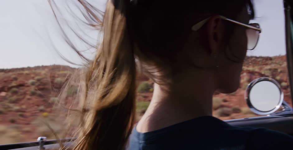 Slow motion close-up of a woman's ponytail blowing in the wind as she drives a convertible on a desert road trip