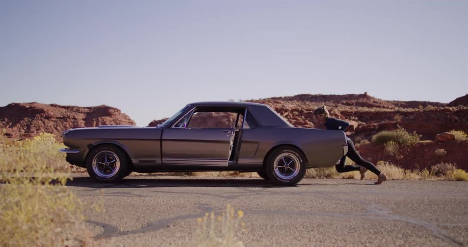 A continuous loop of a determined woman repeatedly trying to push her broken-down classic Mustang on a remote desert highway