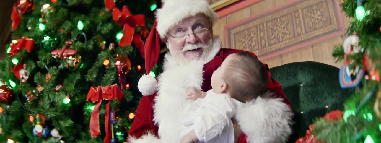 Santa holds a baby on his lap while talking