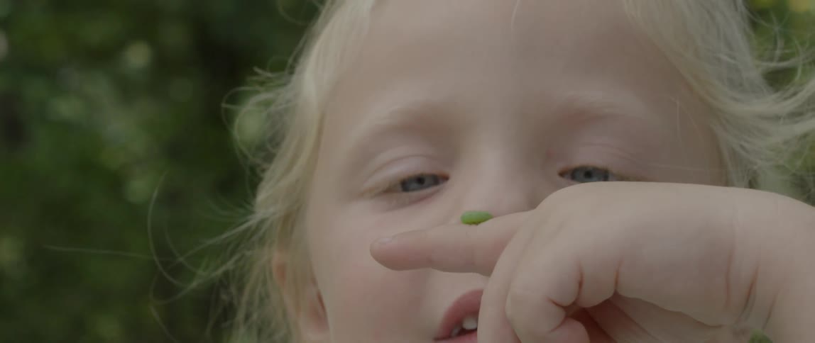 Child watches a green worm crawl on her finger