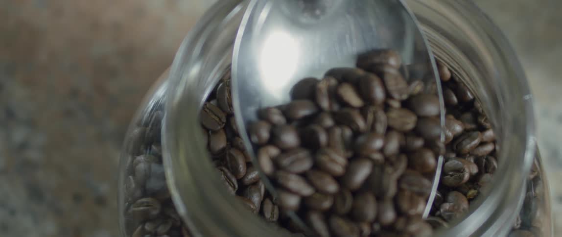 Coffee beans are scooped from a jar