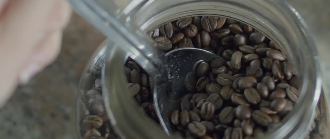 Coffee beans are spooned out of a jar