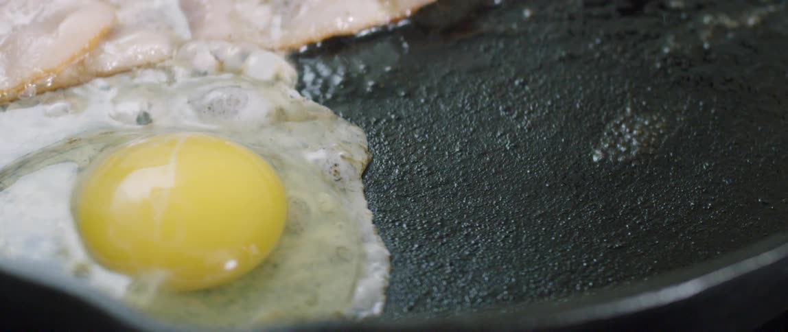 Bacon and eggs are being cooked on a pan