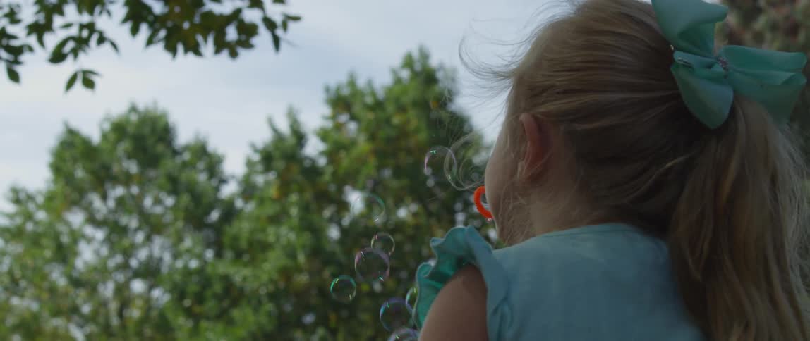 A little girl is blowing bubbles outside during the day