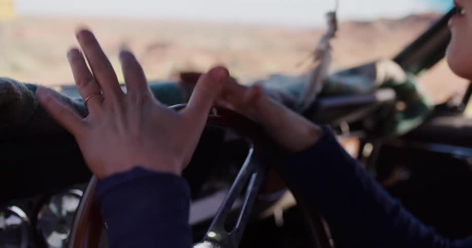 Close up of a driver gesturing excitedly with their hands while navigating a classic car through a sunny landscape