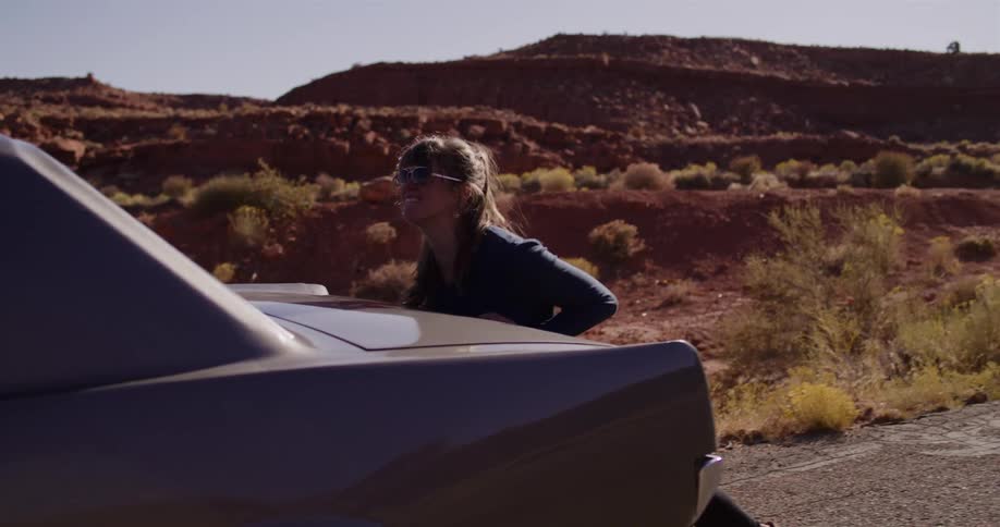 Slow motion shot of a frustrated woman trying to push her vintage car that has broken down on a remote desert road