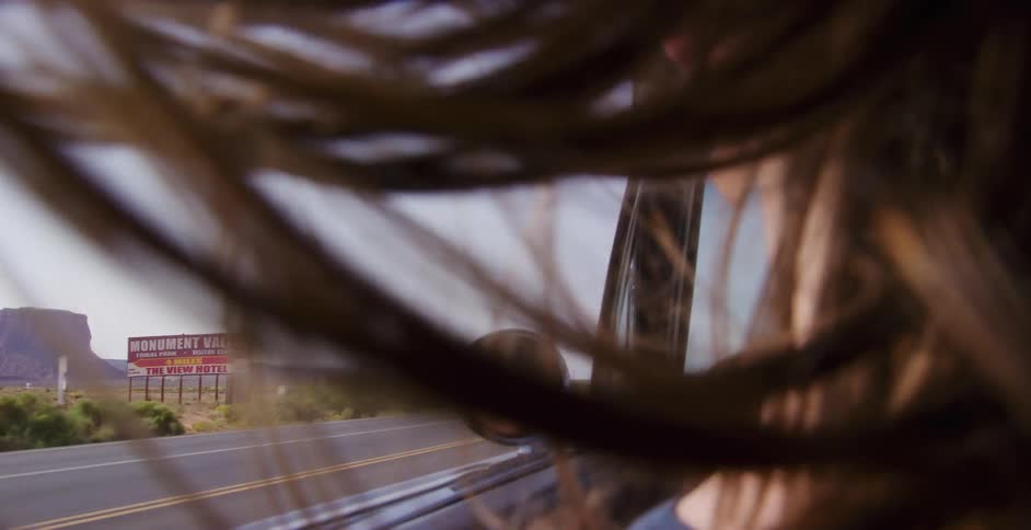 Cinematic slow motion shot of a woman's hair blowing in the wind on a road trip through Monument Valley, with her face reflected in the side mirror