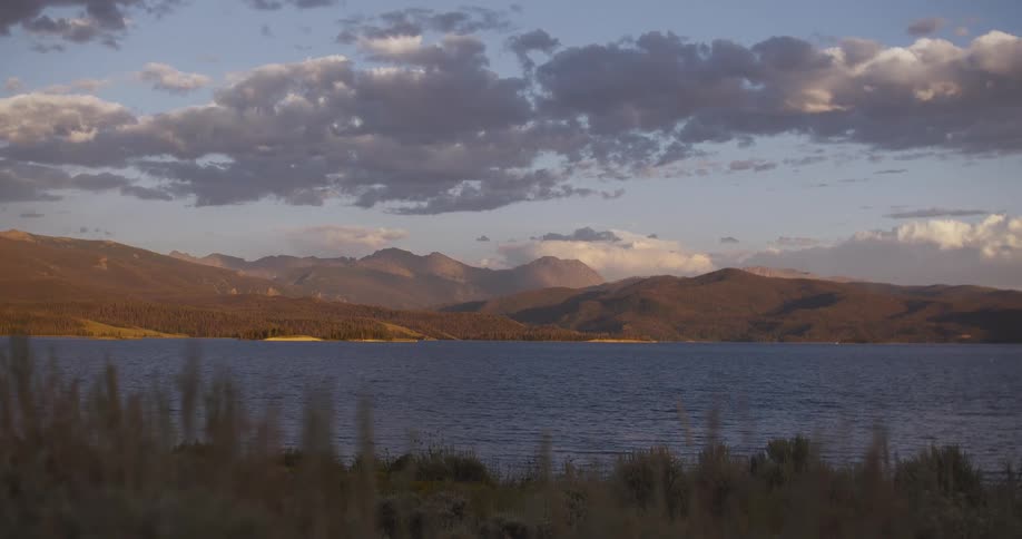 A tranquil wide shot of a beautiful mountain lake at dusk under a cloudy sky