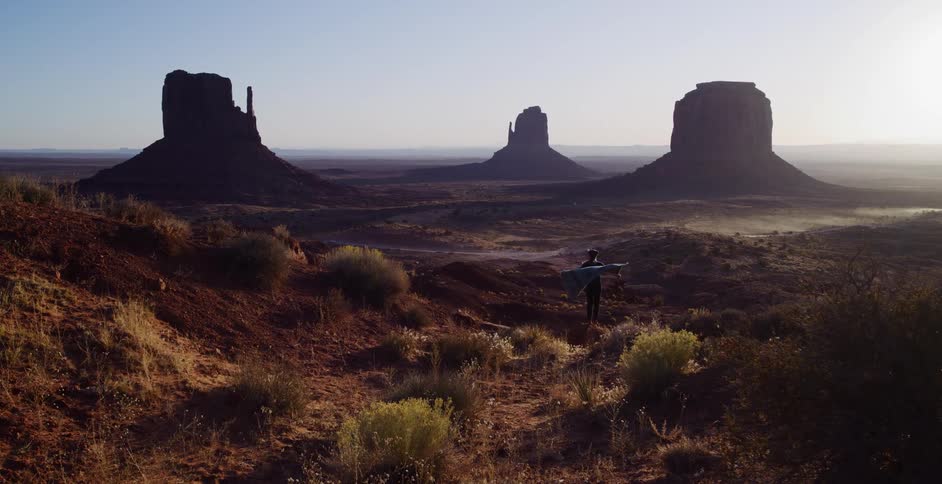 A lone figure performs a tree pose yoga stretch with a flowing blanket in the vast desert landscape of Monument Valley at sunrise