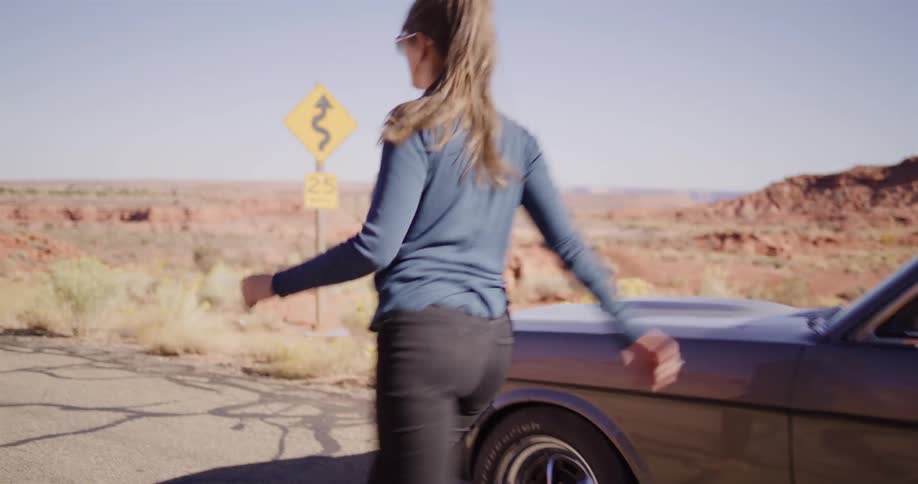 A woman on a desert road trip gets out of her classic Mustang to open the hood after it breaks down