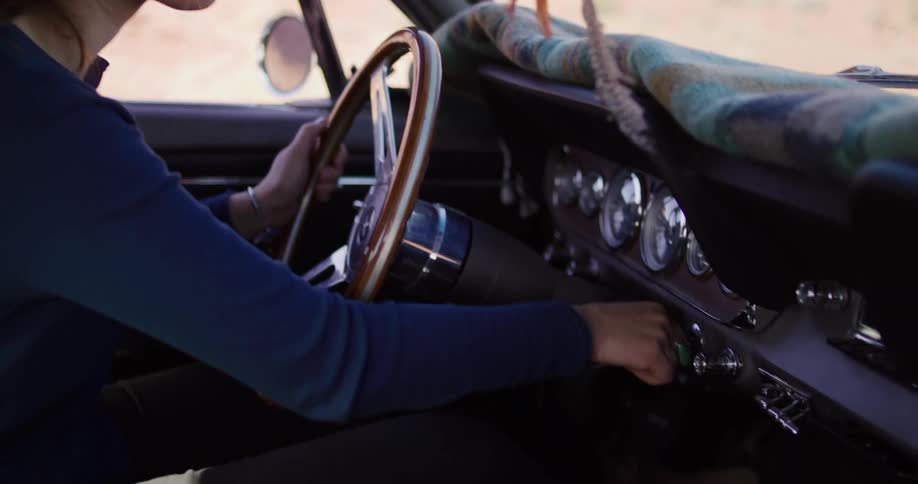 A woman in sunglasses smiles as she successfully starts the ignition of her classic vintage car