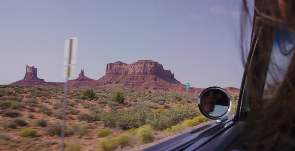 Slow motion shot from inside a car of a woman's hair blowing in the wind with the iconic red rock formations of Monument Valley in the background