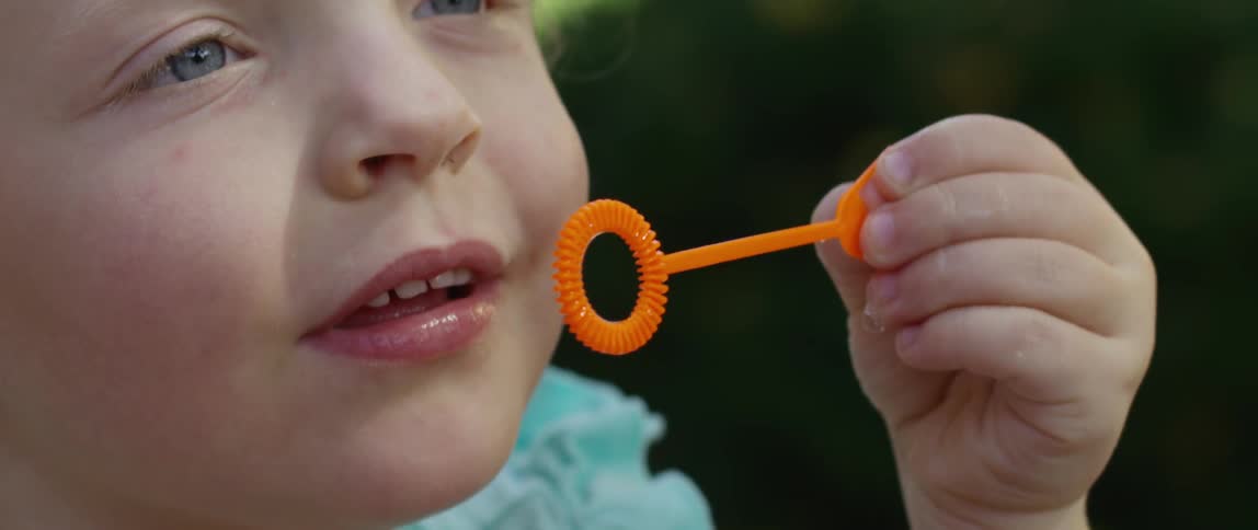 A young girl blows bubbles using a bubble wand