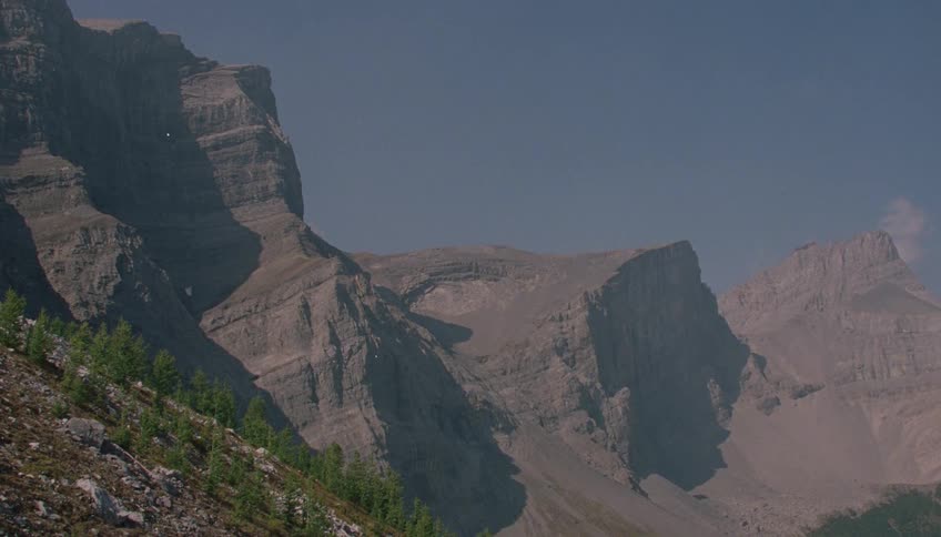 A majestic, rugged mountain range stands against a clear, hazy blue sky