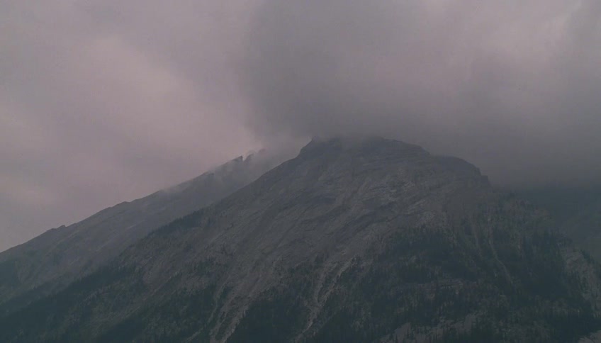 A static shot of a rugged mountain peak enveloped in dark, stormy clouds as rain begins to fall